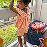 Yazmin joined the competition — help win amazing prizes! toddler, child, window, curious, peach_outfit, standing, indoors, toys, basket, greenery, expression, hair, shoe, sill, playroom, daylight, looking, person, home, casual