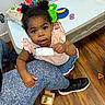 toddler, child, cup, toy, play_table, animal_hospital_toy, wooden_floor, leggings, sneakers, hair_buns, indoor, person, curious, looking_up, holding, small_cup, colorful_toys, playtime, floor, casual_clothing