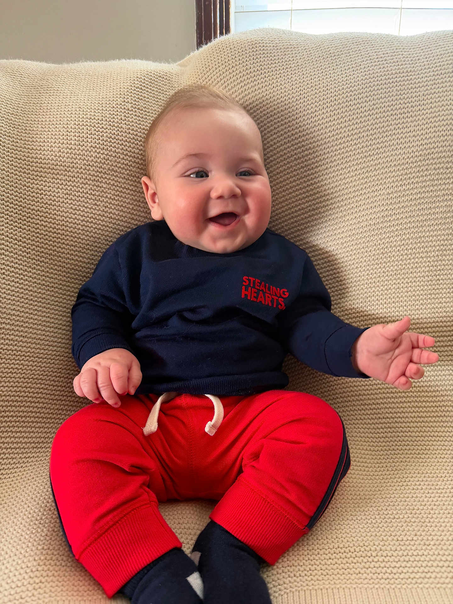 Ryder joined the competition — help win amazing prizes! baby, infant, child, smiling, couch, knit_blanket, navy_sweater, red_pants, socks, hands, face, portrait, indoor, window, cozy, happy, cheeks, seat, clothing, soft_texture