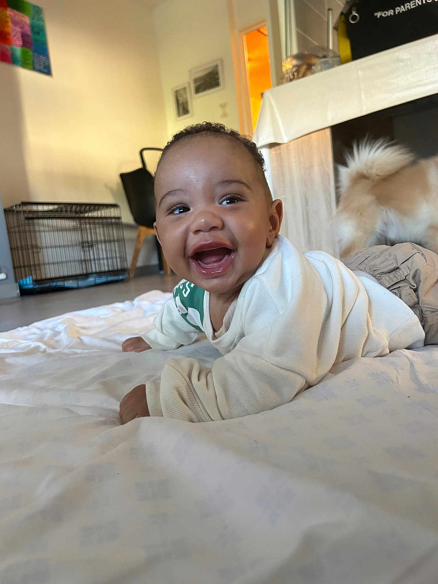 Loyal participe au concours pour gagner de l'argent avec cette photo : baby, smiling, indoor, blanket, happy, child, lying_down, dog_tail, furniture, floor, white_clothing, portrait, home, cute, toddler, playful, person, cheerful, room, casual