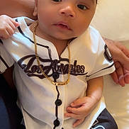 Loyal participe au concours pour gagner de l'argent avec cette photo : baby, baseball_jersey, black_and_white, casual, child, clothing, curly_hair, cute, gold_chain, hand, indoor, infant, jewelry, lap, person, portrait, shorts, sitting, skin, young