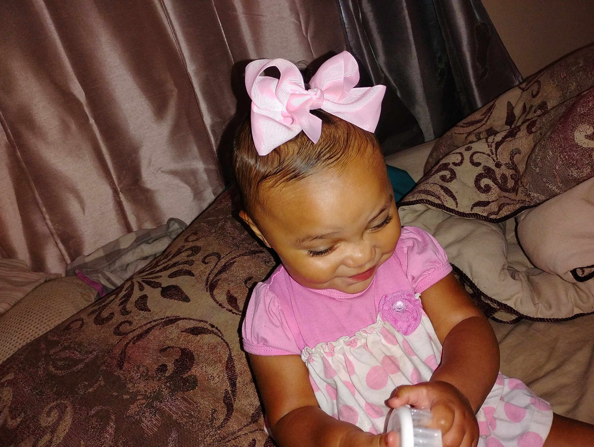 Myla joined the competition — help win amazing prizes! toddler, child, pink_bow, polka_dot_dress, smiling, indoors, pillows, curtains, happy, playing, person, baby, cute, seated, fabric, home, toy, hand, face, closeup