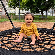 Ines participe au concours pour gagner de l'argent avec cette photo : toddler, child, playground, swing, rope_swing, smiling, barefoot, yellow_shirt, outdoor, grass, tree, bench, wood_chips, residential_building, happy, person, daylight, park, seat, nature