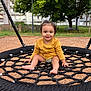 toddler, child, playground, swing, rope_swing, smiling, barefoot, yellow_shirt, outdoor, grass, tree, bench, wood_chips, residential_building, happy, person, daylight, park, seat, nature
