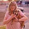 Sawyer is registered to the contest to win money with this photo: woman, dog, pet, outdoor, sunset, smiling, glasses, pink_dress, holding, small_dog, happy, portrait, urban, sidewalk, tree, casual, nature, evening, blurred_background, friendly