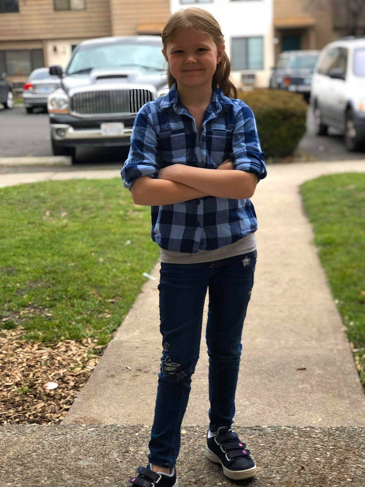 Harlie is registered to the contest to win money with this photo: asphalt, car, denim, face, footwear, glasses, grass, jeans, joy, land_vehicle, person, plaid, plant, road_surface, sidewalk, street_fashion, tartan, tire, tree, vehicle