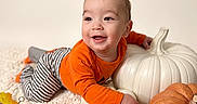 Matteo is registered to the contest to win money with this photo: baby, child, smiling, autumn, pumpkins, orange_shirt, striped_pants, zebra_stripes, indoor, portrait, crawling, happy, infant, face, playful, fall_leaves, blanket, seasonal_decor, still_life, photography