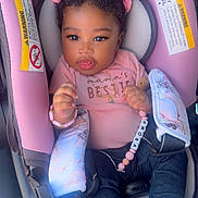 Amora is registered to the contest to win money with this photo: baby, child, car_seat, pink, clothing, hair_bow, hair_clip, denim, shoes, bracelet, necklace, infant, cute, portrait, indoor, seat_belt, accessory, person, smiling, young