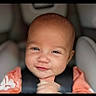 baby, infant, child, portrait, smiling, sitting, car_seat, vehicle, harness, clothing, orange_shirt, face, eyes, hair, head, indoor, close_up, photograph, happy, safe