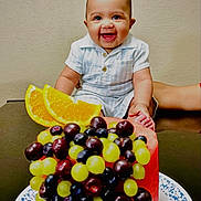 Nile is registered to the contest to win money with this photo: baby, blueberries, child, clothing, colorful, cute, food, fruit, grapes, happy, healthy, indoor, infant, orange_slices, person, plate, portrait, smile, table, watermelon