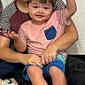 carpet, casual_clothing, child, family, glasses, happy, holding, indoor, interaction, people, person, portrait, seated, shirt, shorts, smile, socks, toddler, wall, young