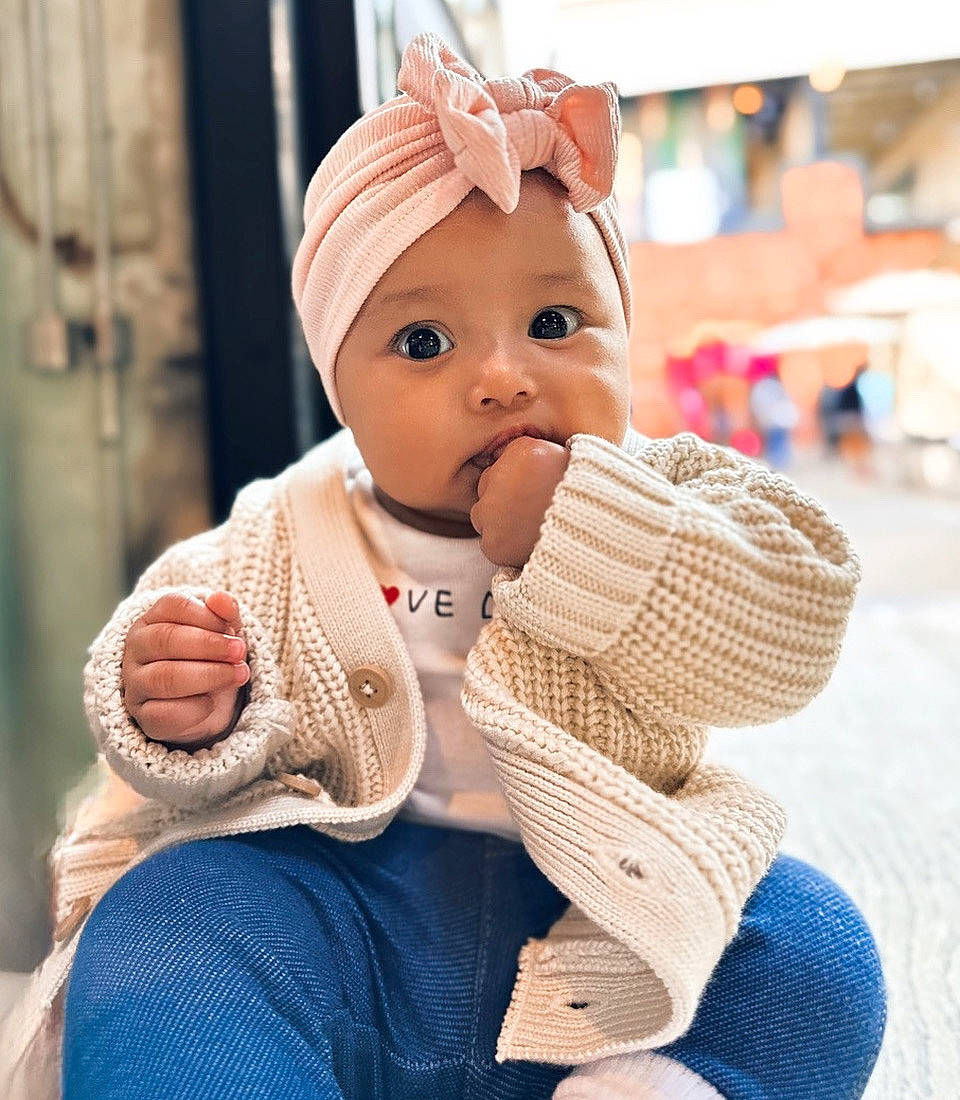 Emma is registered to the contest to win money with this photo: baby, baby_toddler_clothing, beauty, cap, child, curtain, eye, fashion_accessory, fun, glove, happy, headwear, knit_cap, leisure, person, sitting, skin, sleeve, thumb, toddler