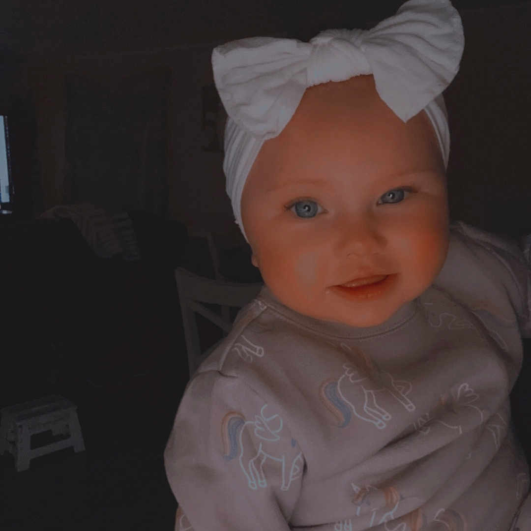Vayda is registered to the contest to win money with this photo: baby, bodypart, bonnet, clothing, couch, dress, face, fashion, finger, formalwear, gown, hand, hardwood, hat, head, person, photography, portrait, toy, wood