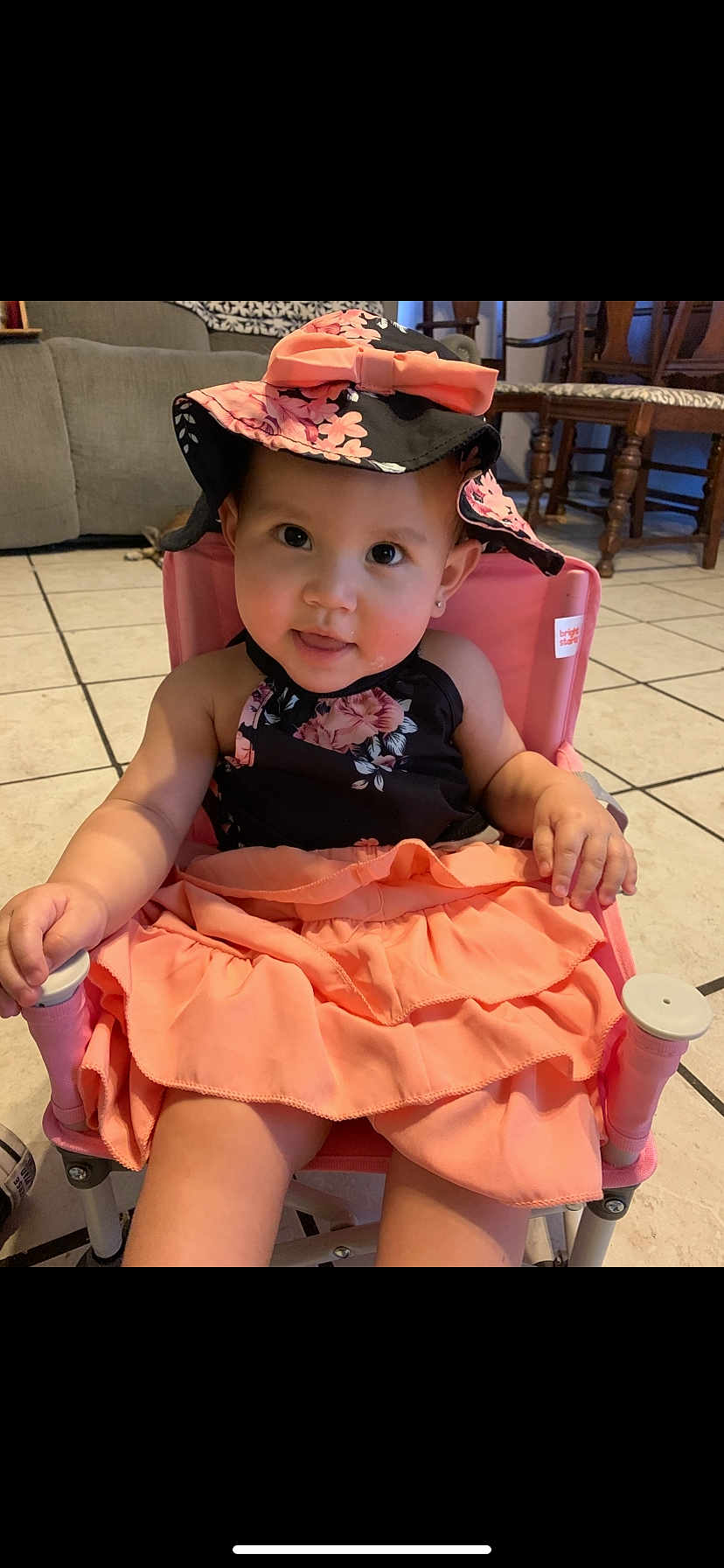 Ivonne is registered to the contest to win money with this photo: baby, black, chair, child, curious, cute, dress, earrings, face, floral_pattern, furniture, hat, indoor, person, pink, portrait, sitting, smiling, tiled_floor, young_child