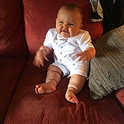 Jax is registered to the contest to win money with this photo: baby, child, infant, couch, red_couch, white_clothing, cute, smiling_face, funny_face, plush, cushion, indoors, person, barefoot, seated, chubby, home, fabric, casual, furniture