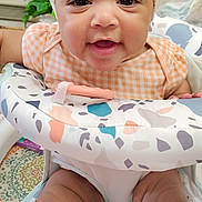 Gianna is registered to the contest to win money with this photo: baby, infant, headband, smiling, sitting, patterned, baby_seat, clothing, face, legs, happy, indoor, child, person, cute, colorful, home, decor, plant, toddler