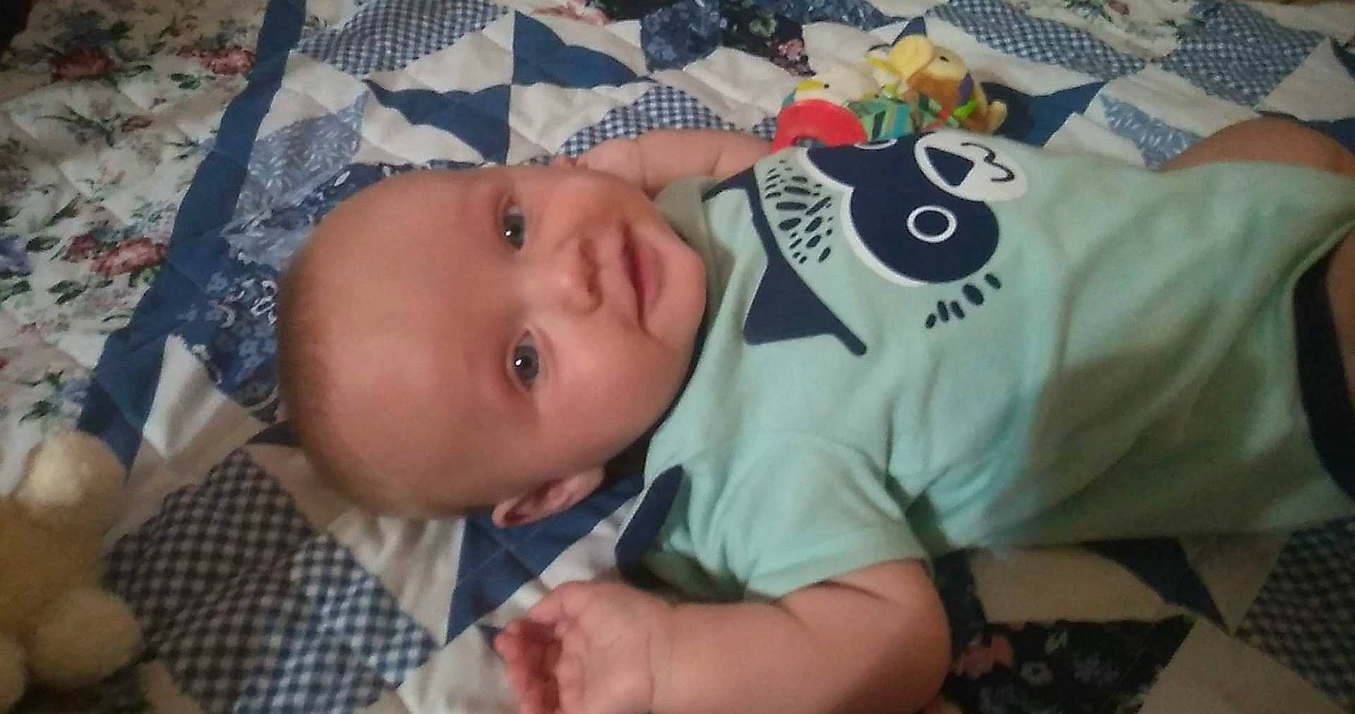 Bradley is registered to the contest to win money with this photo: baby, baby_products, baby_toddler_clothing, cheek, child, facial_expression, finger, fun, grass, happy, iris, linens, mouth, pattern, person, plaid, skin, sleeve, t_shirt, tartan