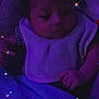 baby, infant, blanket, bib, purple_light, sparkles, face, hand, sleeping_area, child, cute, soft_texture, portrait, dark, indoors, cozy, young, resting, peaceful, person