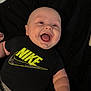 Kannyn is registered to the contest to win money with this photo: baby, infant, smiling, laughing, mouth_open, chubby_cheeks, nike_logo, black_shirt, onesie, arm, lying_down, blanket, bed, indoor, cute, portrait, happy, face, clothing, newborn