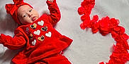 Kimberly is registered to the contest to win money with this photo: baby, infant, red_clothing, headband, heart_pattern, blanket, flower_petals, christmas_tree, ornaments, holiday, floor_tiles, foot, decorations, cute, lying_down, indoor, holiday_theme, festive, soft_texture, child