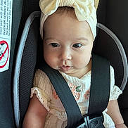 Kimberly is registered to the contest to win money with this photo: baby, infant, child, car_seat, seat_belt, headband, bow, dress, embroidery, pink, white, face, eyes, skin, arm, hand, fabric, sitting, cute, sunlight