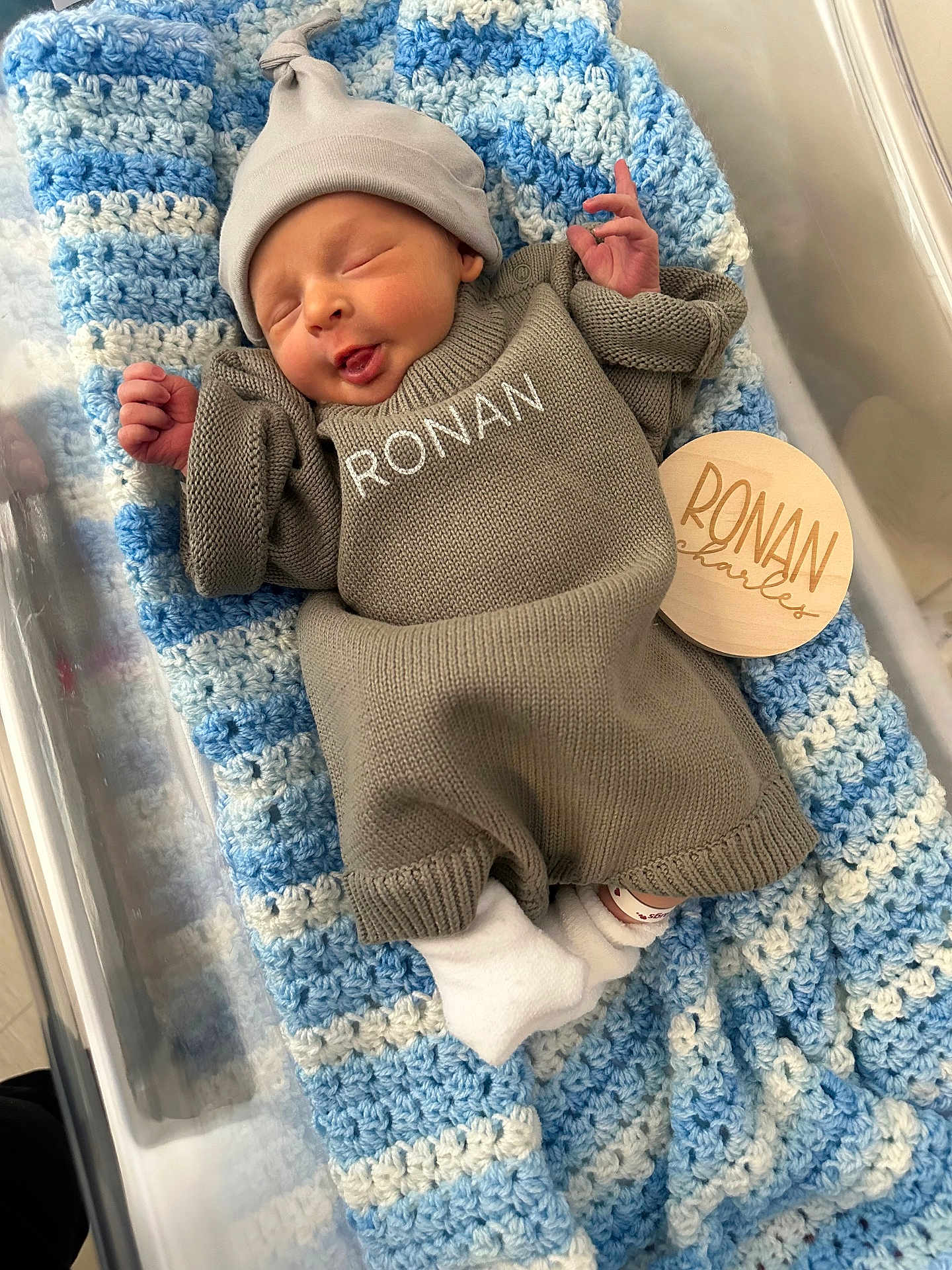 Ronan is registered to the contest to win money with this photo: newborn, baby, infant, blanket, bassinet, beanie, knit_sweater, name_on_clothing, wooden_name_tag, crocheted_blanket, smile, sleeping, hospital_id_band, sock, cozy, soft_texture, portrait, cute, hand, nursery
