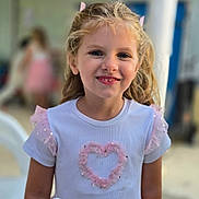 Lya a rejoint le concours — aidez-le/la à gagner de superbes lots ! child, girl, smiling, blonde_hair, white_dress, pink_heart, ruffles, hair_bows, portrait, indoor, happy, cute, young, face, person, fashion, childhood, innocence, joy, casual