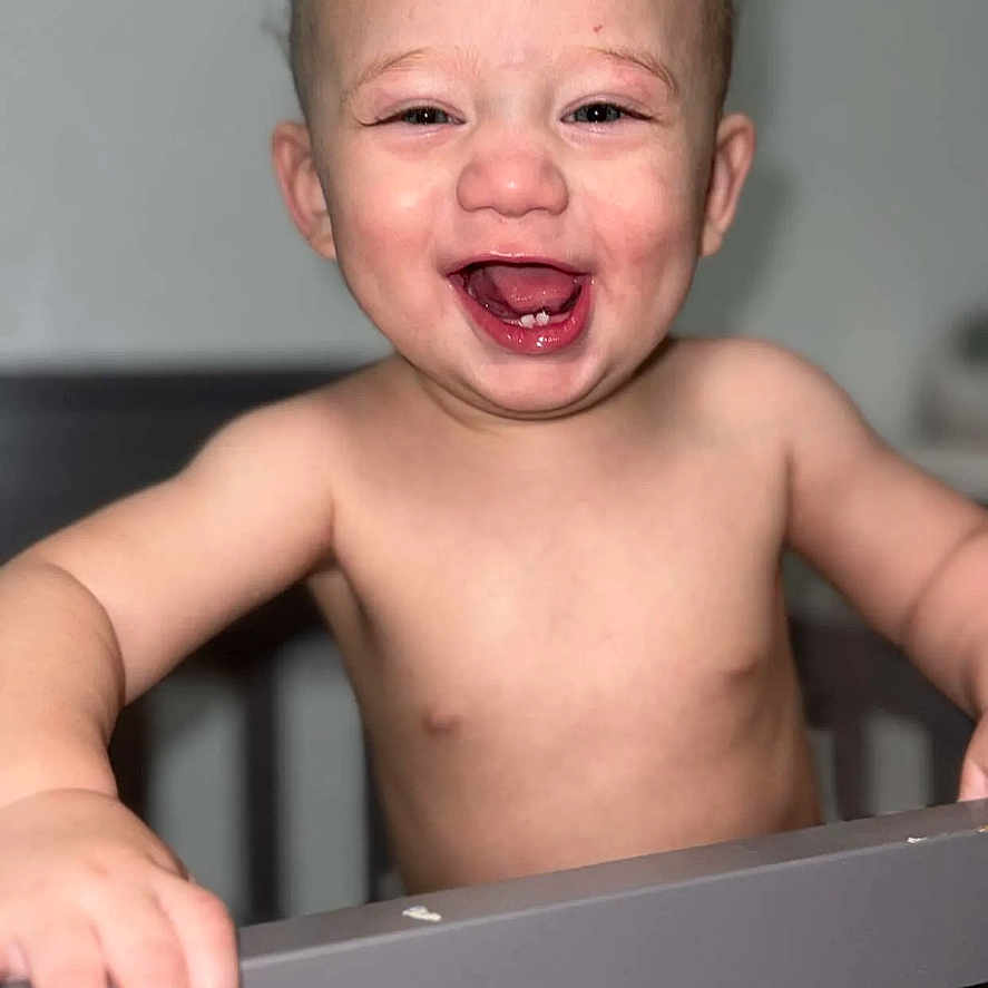 Emmett is registered to the contest to win money with this photo: toddler, child, baby, crib, laughing, happy, smiling, bare_chest, indoor, portrait, face, person, young_child, infant, hand, skin, hair, room, closeup, joyful