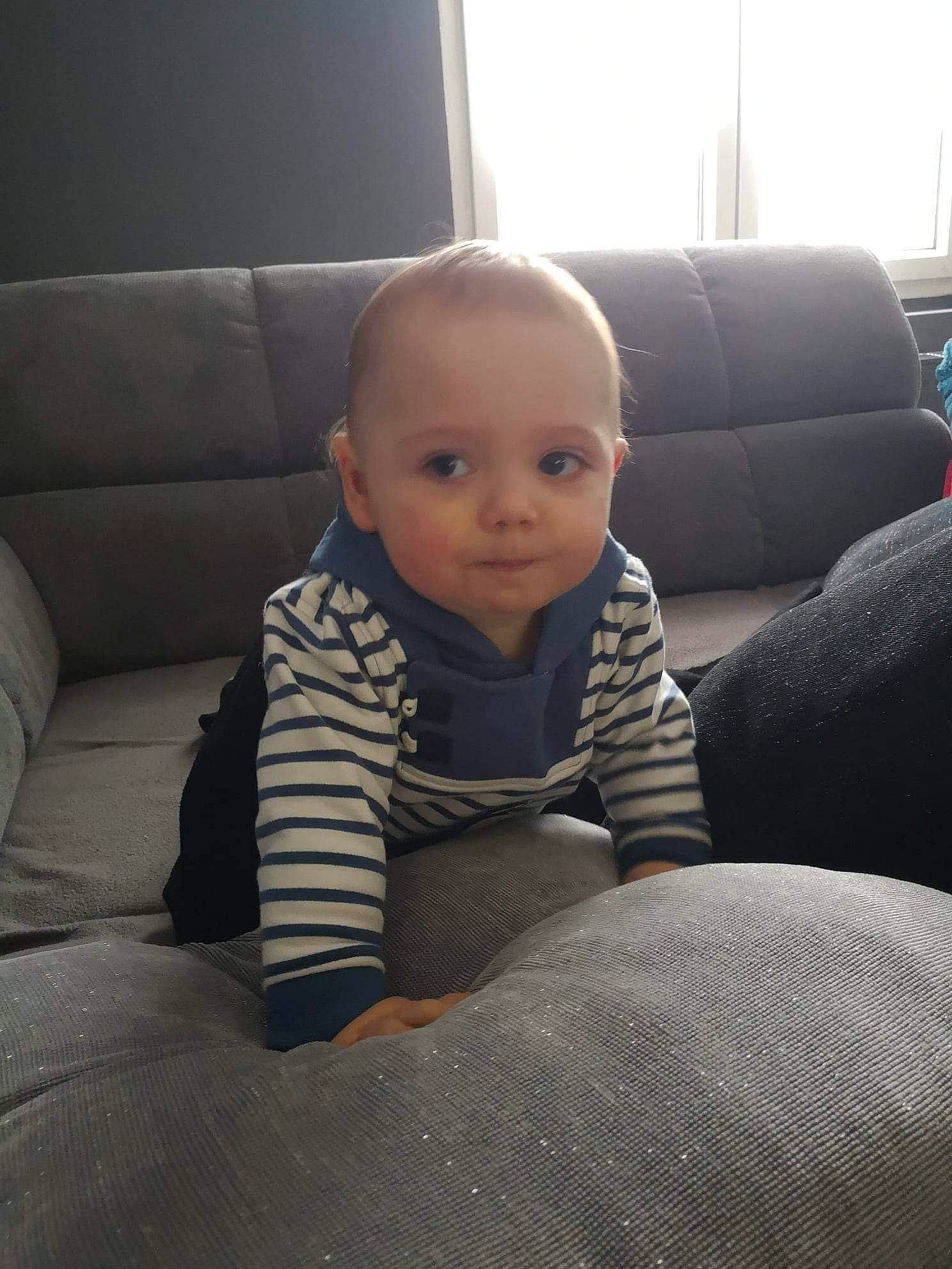 Milan a rejoint le concours — aidez-le/la à gagner de superbes lots ! baby, baby_toddler_clothing, child, comfort, couch, eye, floor, flooring, fun, hardwood, human_leg, knee, living_room, person, room, sitting, tints_and_shades, toddler, window, window_blind