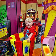 Tucker joined the competition — help win amazing prizes! child, amusement_ride, arcade, indoor, colorful, blonde_hair, smiling, red_shirt, play, fun, game, seat, entertainment, happy, young, patterned_carpet, toy, person, bright_colors, leisure