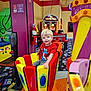 child, amusement_ride, arcade, indoor, colorful, blonde_hair, smiling, red_shirt, play, fun, game, seat, entertainment, happy, young, patterned_carpet, toy, person, bright_colors, leisure