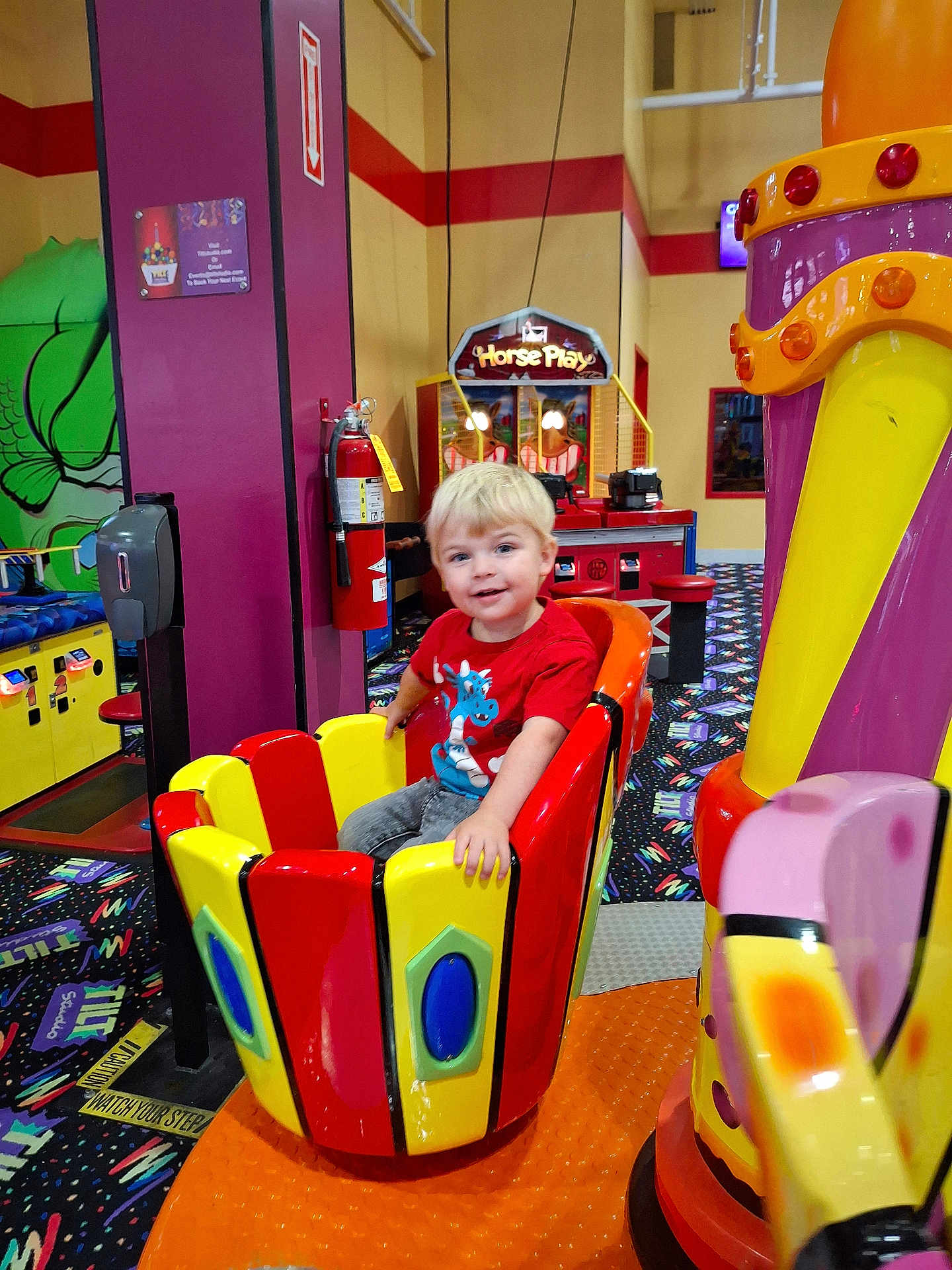 Tucker joined the competition — help win amazing prizes! child, amusement_ride, arcade, indoor, colorful, blonde_hair, smiling, red_shirt, play, fun, game, seat, entertainment, happy, young, patterned_carpet, toy, person, bright_colors, leisure