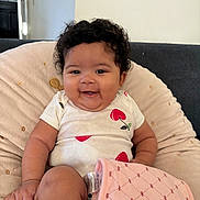 Nevaeh joined the competition — help win amazing prizes! baby, child, smile, curly_hair, onesie, cherries, blanket, cushion, indoor, happy, sitting, person, infant, face, cute, cozy, joyful, furniture, home, portrait