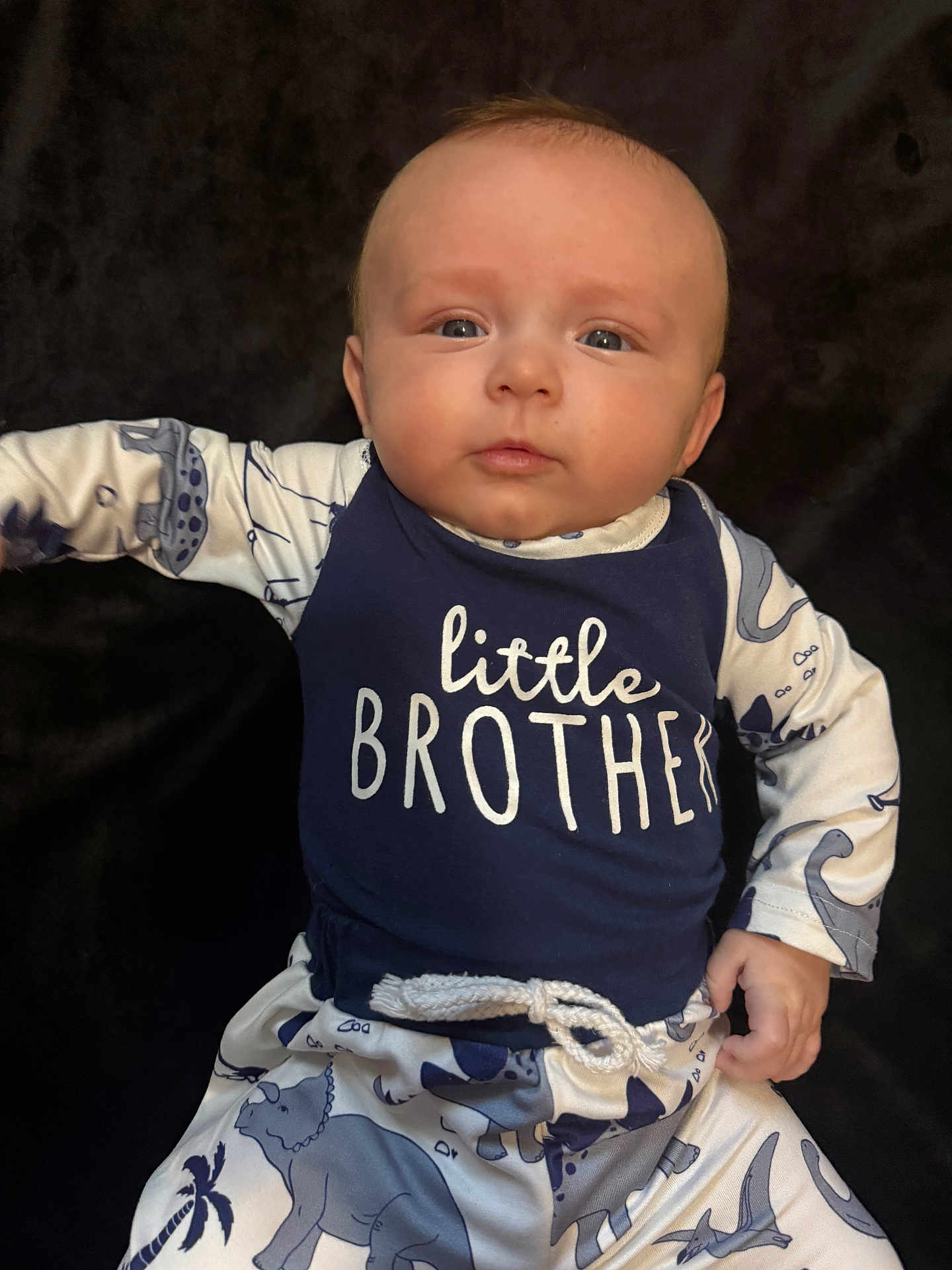 Waylon joined the competition — help win amazing prizes! baby, infant, child, face, blue_clothing, pajamas, dinosaur_print, lying_down, hand, expression, portrait, young, cute, childrens_clothing, sleeves, rope_belt, dark_background, looking, person, skin