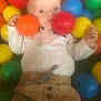 baby, child, colorful_balls, ball_pit, toy, play, infant, face, clothing, white_shirt, brown_pants, indoor, soft_focus, cute, hand, expression, round_objects, bright_colors, person, young_child