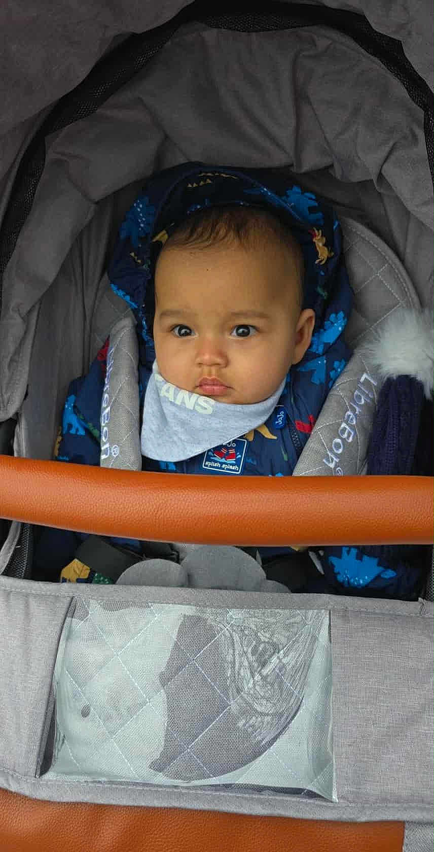 Chearlie joined the competition — help win amazing prizes! baby, child, stroller, jacket, hood, face, infant, clothing, blue, dinosaur_pattern, blanket, seatbelt, portrait, person, cute, bundle, outdoor, warm, expression, wide_eyes