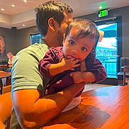 Lakshmi joined the competition — help win amazing prizes! arm, baby, background, casual_clothing, child, curious, exit_sign, face, fingers, hair, holding, indoor, lighting, man, person, restaurant, seat, table, window, wooden_table