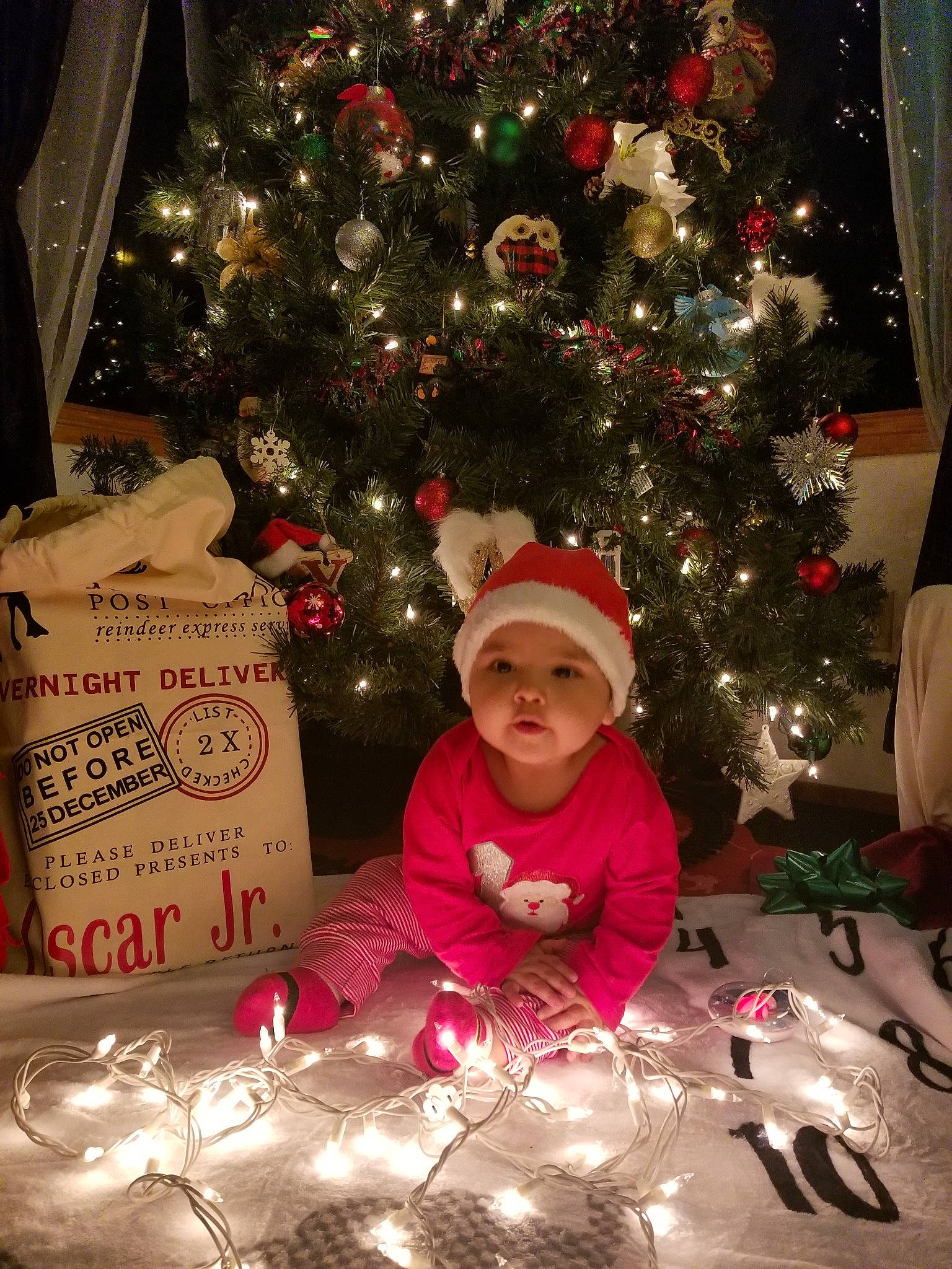 Oscar Jr. is registered to the contest to win money with this photo: child, christmas, christmas_decoration, christmas_eve, christmas_lights, christmas_ornament, christmas_tree, conifer, event, fir, headwear, holiday, holiday_ornament, interior_design, ornament, person, pine_family, plant, toddler, tree