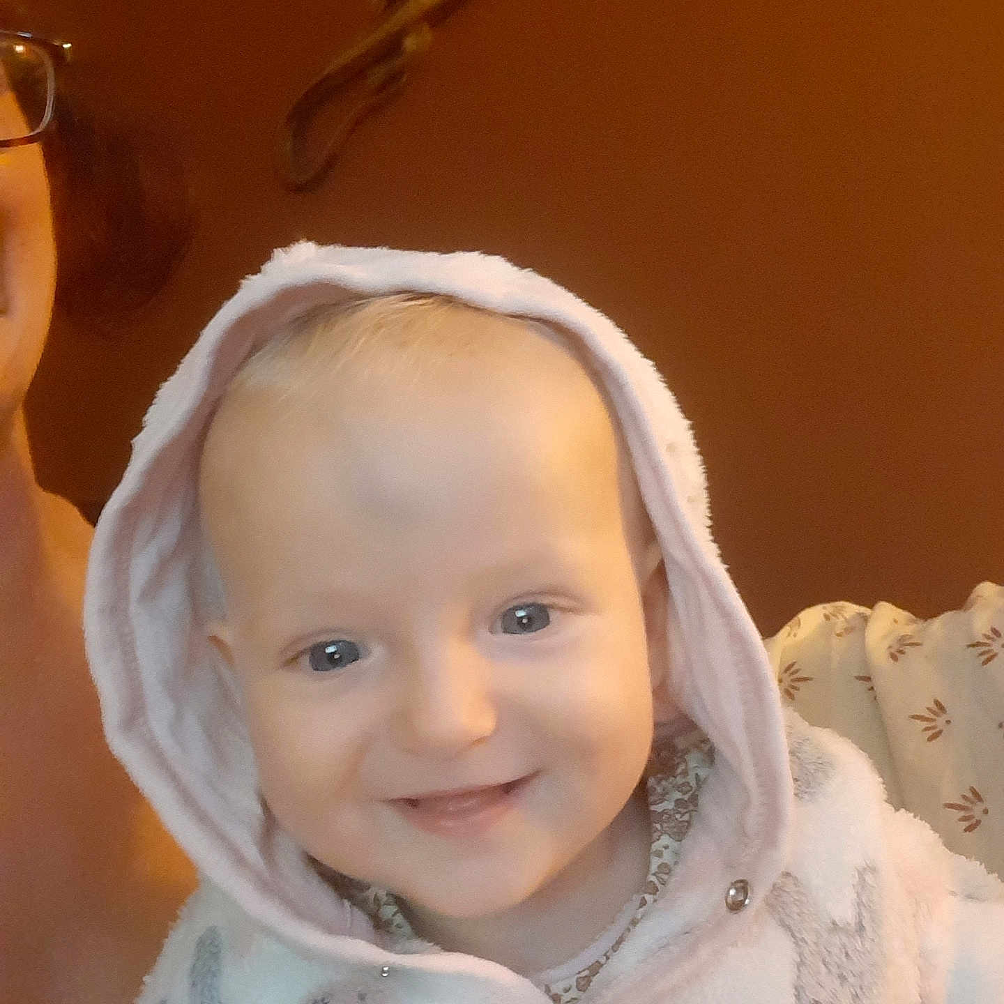 Iris participe au concours pour gagner de l'argent avec cette photo : adult_partial, baby, background, child, closeup, clothing, cozy, cute, eyes, face, happy, hood, indoor, infant, jacket, person, portrait, skin, smile, warm_lighting