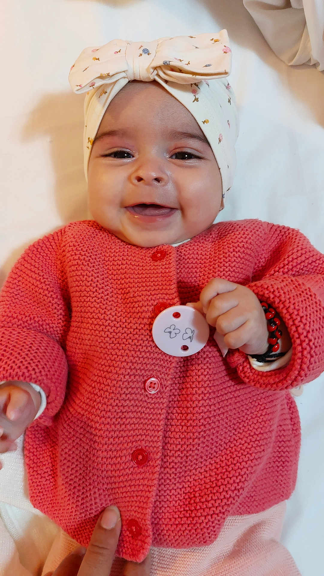 Sofiana participe au concours pour gagner de l'argent avec cette photo : baby, smiling, headband, pink_sweater, button, hand, infant, cute, lying_down, happy, face, skin, clothing, knitted, person, child, cozy, accessory, soft, portrait