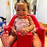 Jaxlynn joined the competition — help win amazing prizes! baby, child, smile, dimples, curly_hair, red_baby_seat, foot, hand, pink_dress, indoors, kitchen, person, cute, happy, seated, infant, home, furniture, table, light