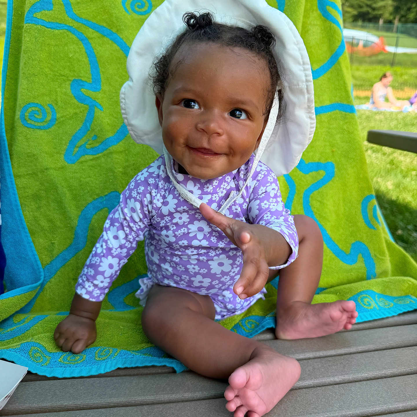 Jaxlynn is registered to the contest to win money with this photo: toddler, child, smiling, purple_clothing, sunhat, curly_hair, dolphin_towel, bench, outdoor, green_towel, grass, daylight, cute, baby, happy, reaching_hand, park, summer, playful, portrait