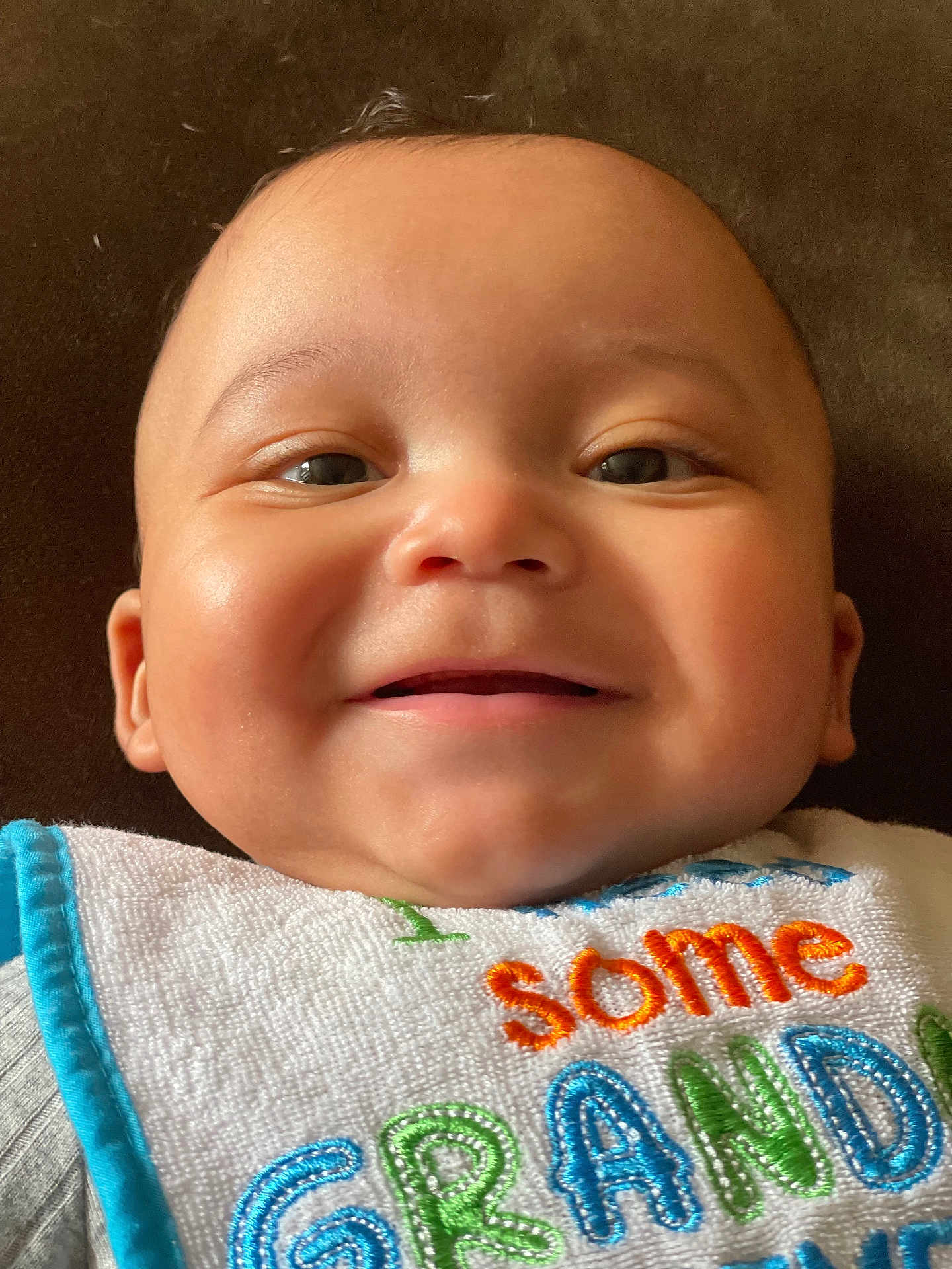 Owen is registered to the contest to win money with this photo: baby, smiling, face, closeup, bib, embroidery, child, infant, cute, happy, skin, person, head, young, mouth, eyes, clothing, texture, colorful, portrait