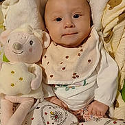 Romy participe au concours pour gagner de l'argent avec cette photo : adorable, baby, bed, bib, blanket, child, clothing, comfort, cozy, cute, face, hand, indoor, infant, lying_down, patterned_blanket, plush_toy, smiling, soft_toy, young