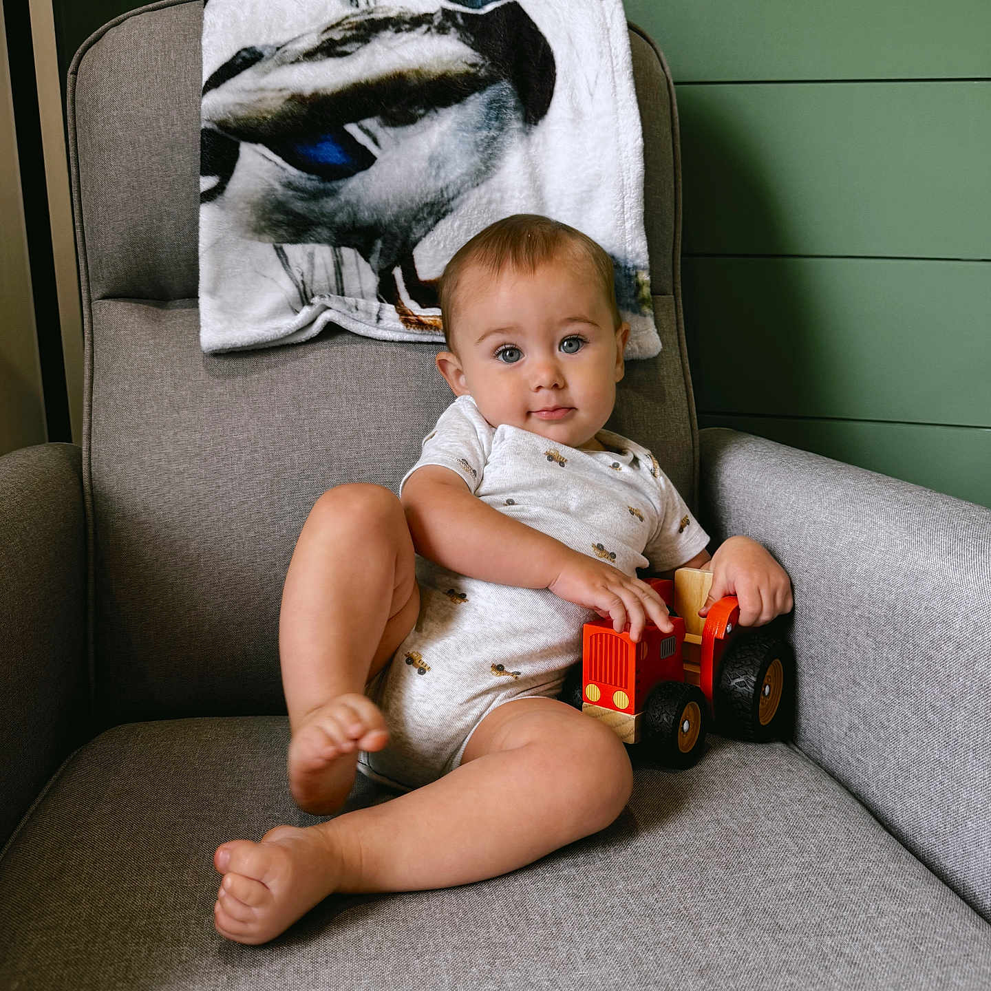 Wesley is registered to the contest to win money with this photo: armchair, baby, blanket, blue_eyes, child, clothing, cute, furniture, green_wall, home, indoor, person, playful, portrait, relaxed, short_hair, sitting, smiling, toy, truck
