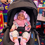 Aleena joined the competition — help win amazing prizes! arcade, baby, baby_carrier, carpet, child, chuck_e_cheese, colorful, entertainment, happy, indoor, infant, mascot, pink_bow, pink_outfit, play_center, portrait, safety_harness, seated, smiling, stroller