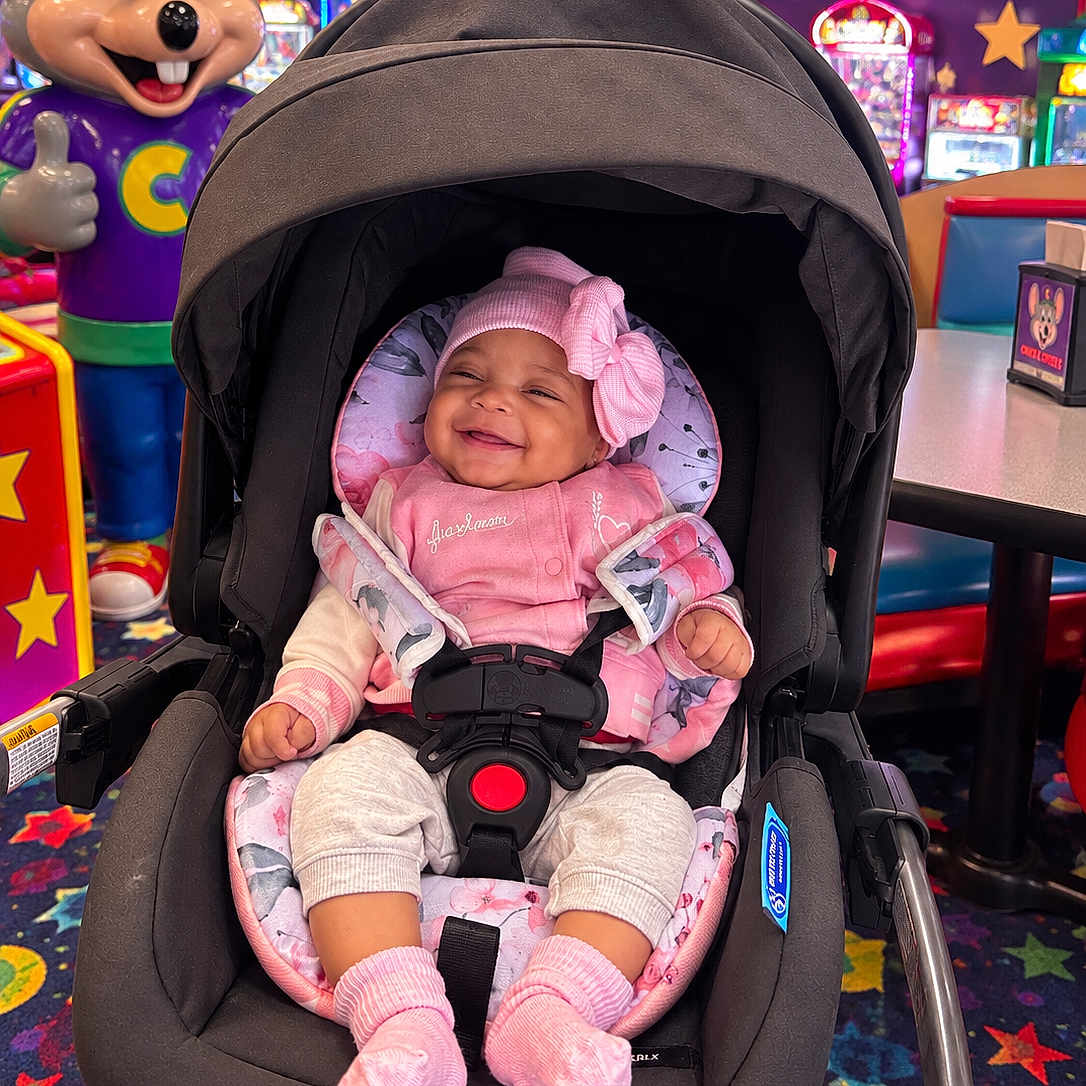 Aleena joined the competition — help win amazing prizes! arcade, baby, baby_carrier, carpet, child, chuck_e_cheese, colorful, entertainment, happy, indoor, infant, mascot, pink_bow, pink_outfit, play_center, portrait, safety_harness, seated, smiling, stroller