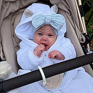 Lainey is registered to the contest to win money with this photo: baby, infant, stroller, white_clothing, headband, bow, cute, outdoor, hand, face, blue_eyes, hood, plush, baby_clothes, child, person, blanket, toy_ring, expression, fur