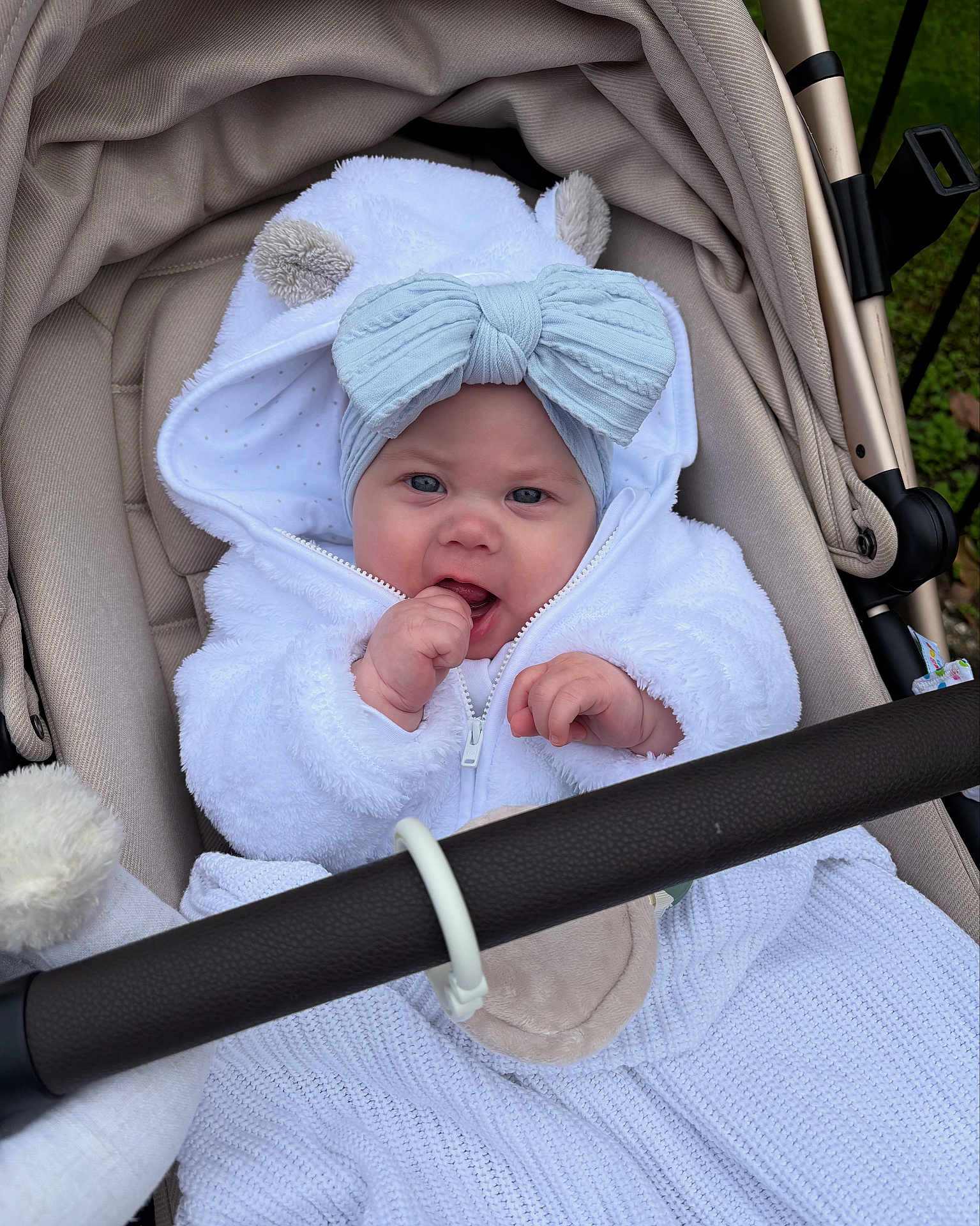 Lainey is registered to the contest to win money with this photo: baby, infant, stroller, white_clothing, headband, bow, cute, outdoor, hand, face, blue_eyes, hood, plush, baby_clothes, child, person, blanket, toy_ring, expression, fur