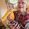 Brayleanna joined the competition — help win amazing prizes! baby, grandfather, child, elderly_man, portrait, smiling, happy, family, holding_baby, indoor, home, red_plaid_shirt, yellow_sweater, glasses, infant, pigtails, furniture, houseplants, sunflowers, photography